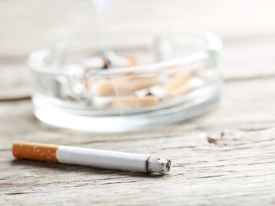 Cigarette with ash on grey wooden table