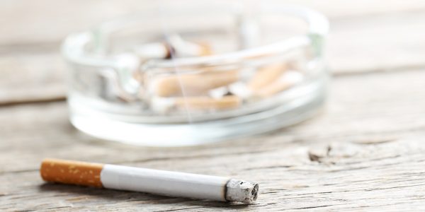 Cigarette with ash on grey wooden table